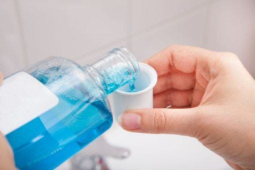 A person pours mouthwash into a small container.