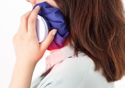 Cropped photo of a woman applying cold pack on one side of her face.