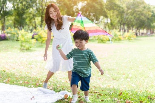 A mom teaching his son how to fly a kite outdoors.