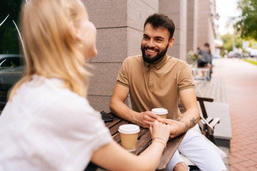 A man and woman having coffee together while the man smiles brightly.