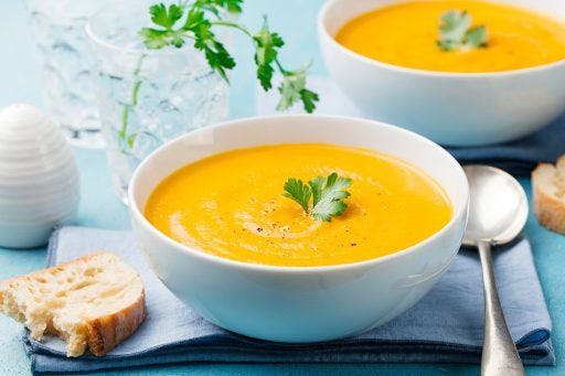 A bowl of pumpkin and carrot soup garnished with parsley.