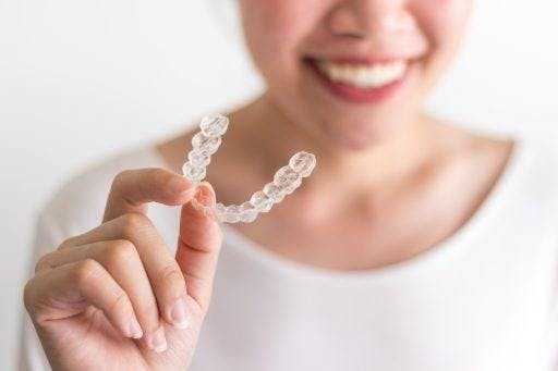 An Asian woman holding invisible aligners.