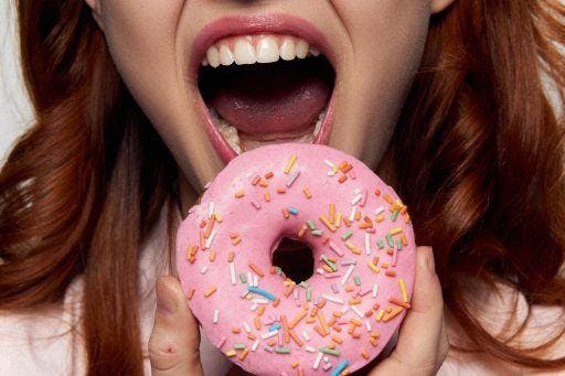 A woman with straight teeth biting into a sprinkle donut.