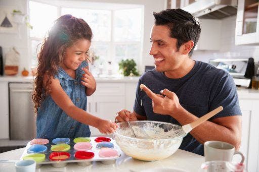 A dad and his daughter preparing cupcakes in the kitchen. 
