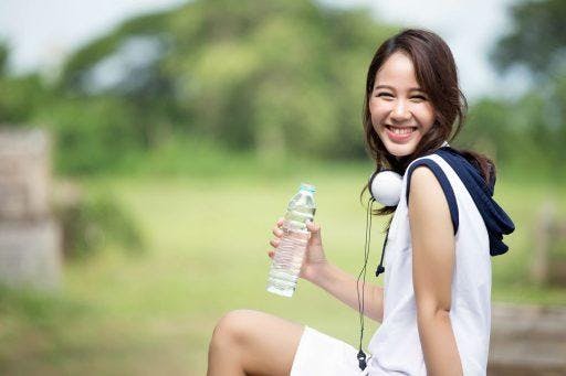 A young woman smiling and sitting outdoors while holding a water bottle. 