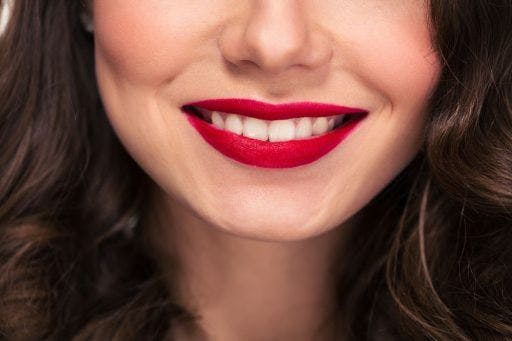Close-up of a woman in red lipstick smiling with teeth.