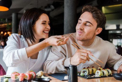 Man and woman holding chopsticks while eating sushi.