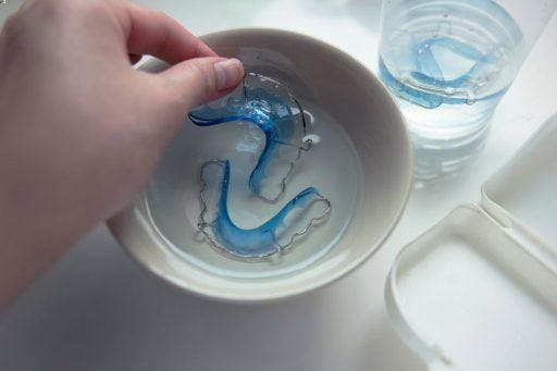 A hand soaking Hawley retainers in a bowl of cleaning liquid.