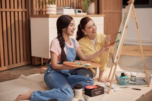 Two smiling women painting on a canvas.