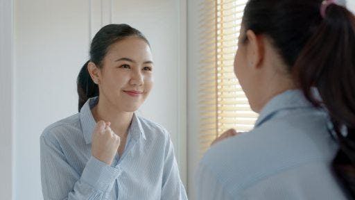 A woman hyping herself up and smiling in front of a mirror.