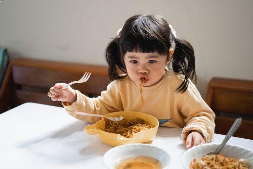 A little girl slurping noodles while holding a fork.