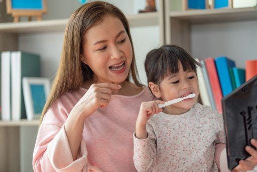 Asian mother teaching her young daughter to brush her teeth.