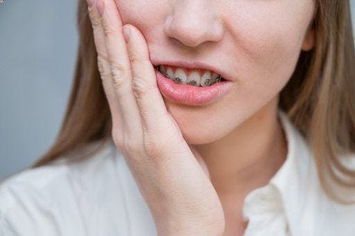 A young girl in braces putting her hand against her cheek, cringing in pain.