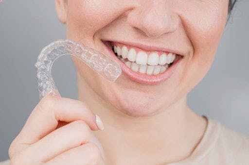 Close-up of a woman with straight teeth holding clear aligners while smiling. 