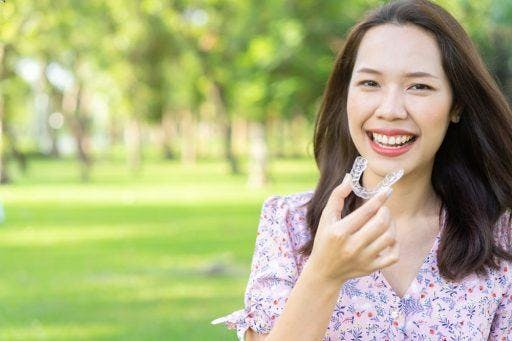 Smiling woman holding a set of clear aligners while walking outdoor.