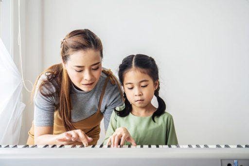 A mother teaching her daughter how to play the piano.