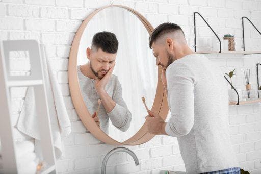 Man holding his cheek in pain while holding a toothbrush.