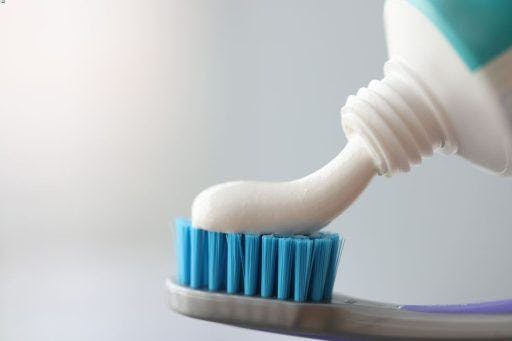 Close-up of toothpaste flowing out of a tube onto a toothbrush.