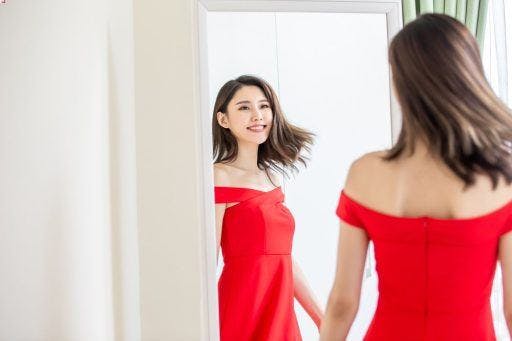 A woman in a red dress smiling in front of the mirror.