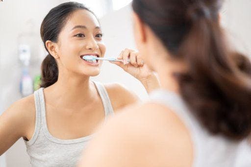 A woman brushing her teeth in front of the bathroom mirror.
