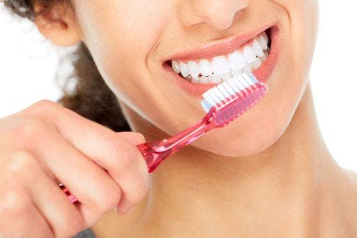 Close-up of a woman smiling while brushing her straight, white teeth.