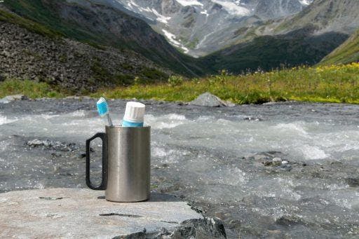 A camping mug with a toothbrush and toothpaste in a scenic landscape.