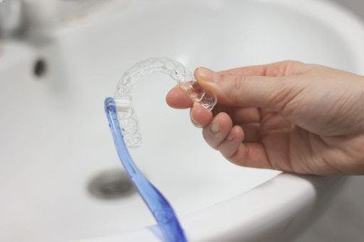 A person cleaning clear aligners with a toothbrush.