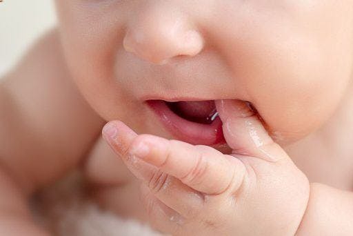 Close-up of a baby sucking and drooling on their fingers.