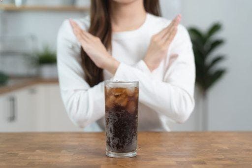 Woman crossing her arms in an “X” shape to signify rejection of an ice-cold glass of soda.