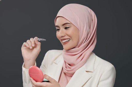 A woman smiling and putting on clear aligners.