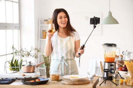 A woman posing with a beverage while using a selfie stick.