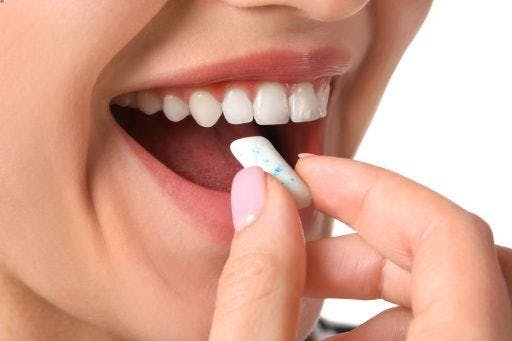 A woman with straight, white teeth about to put a chewing gum tablet in her mouth.