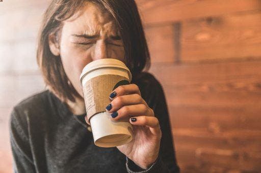 A woman grimacing while sipping hot coffee.