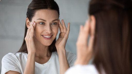 A woman smiling and checking the fine lines around her eyes in the mirror.