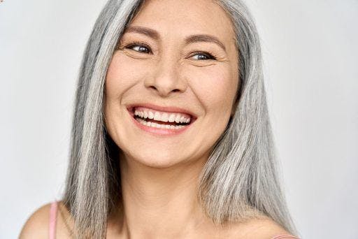 A woman with grey hair smiling with smile lines and crow’s feet.