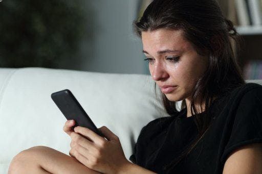 A teenage girl crying while looking at her mobile phone.