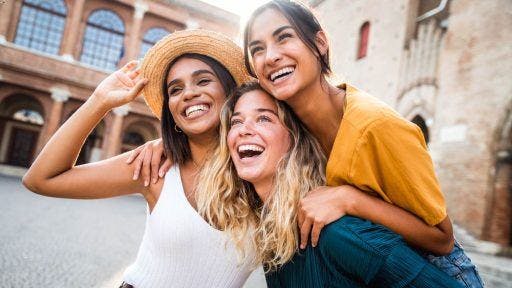 A group of three female friends smiling widely together.