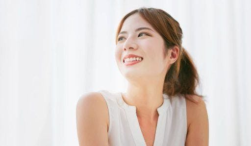 Asian woman in white smiling and looking away against a white background. 