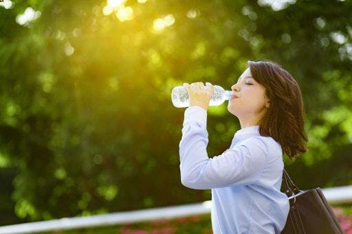 Woman with shoulder-length hair drinking water from a bottle.
