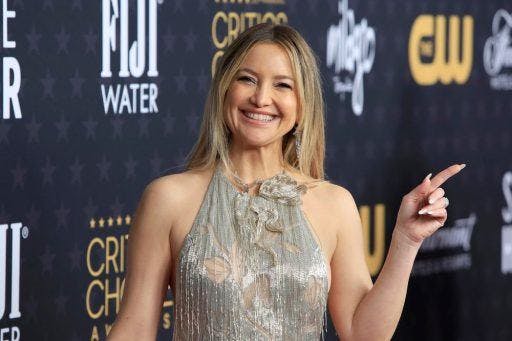 Kate Hudson in green smiling against an event background.