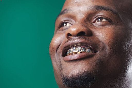 Smiling man of African ethnicity with silver teeth against a green background.