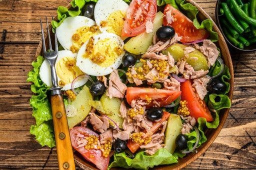 A bowl of niçoise salad with tuna chunks, tomatoes, boiled eggs, and olives.