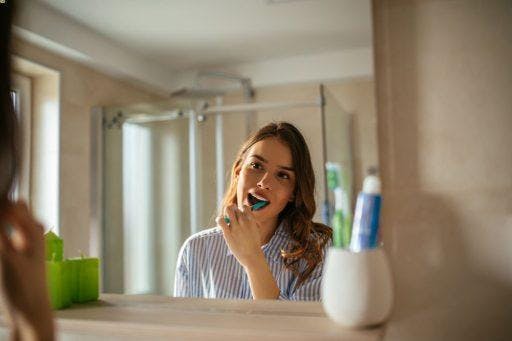 Caucasian woman in stripes brushing her teeth in front of a bathroom mirror.
