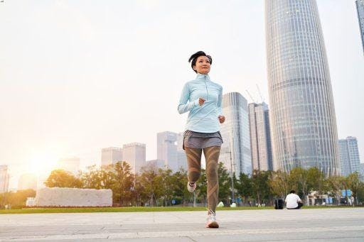 Asian woman with short hair wearing a light blue jacket and workout pants running at a city park.