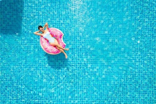 Top view of woman in an inflatable pink donut floating in a swimming pool.