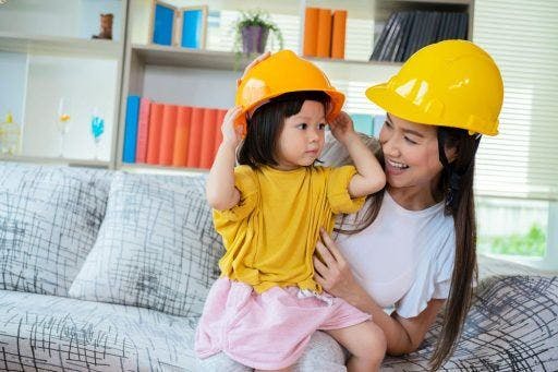 Asian mother and daughter smiling and wearing matching construction hard hats.