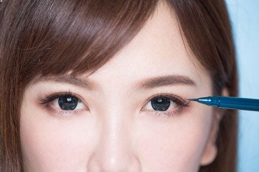 Cropped photo of woman’s eyes and a blue eyeliner pen. 