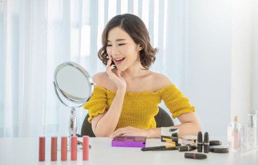 Smiling woman in yellow touching her face and looking in the mirror.