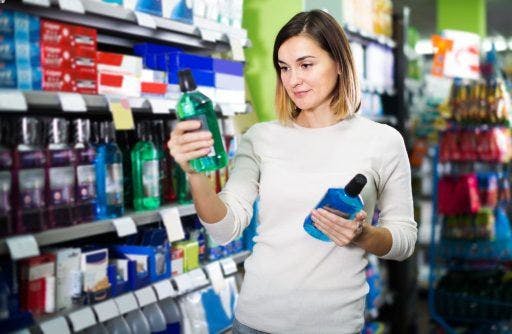 A woman in white looking at two bottles of mouthwash in a store.
