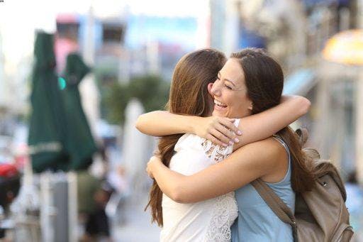 Two women hugging with one of them smiling outdoors.